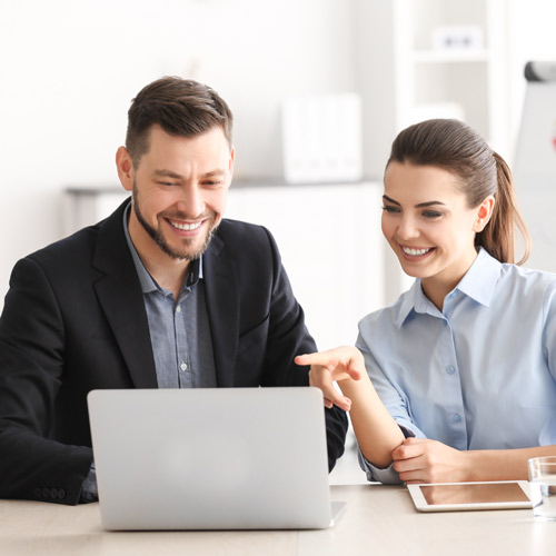 Mann und Frau sitzen vor Laptop und lächeln