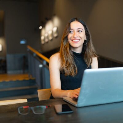 Frau sitzt mit Laptop im Restaurant und sieht lachend zur Seite. Frau sitzt mit Laptop im Restaurant und sieht lachend zur Seite.