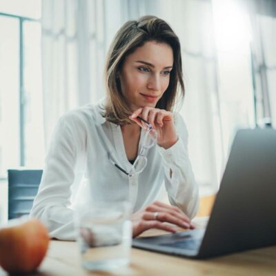 MBA General Management Frau in Bluse sitzt vor Laptop