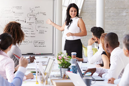 Team Meeting mit Whiteboard, mehrere Frauen und Männer an einem Tisch versammelt